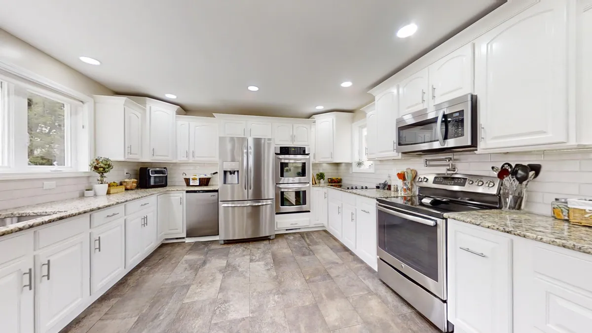 A spacious, well-lit kitchen featuring granite countertops, stainless steel appliances, white cabinetry, and large windows. The scene feels open and welcoming, perfect for group cooking and entertaining. Multiple prep areas and state-of-the-art appliances hint at the kitchen's gourmet capabilities.