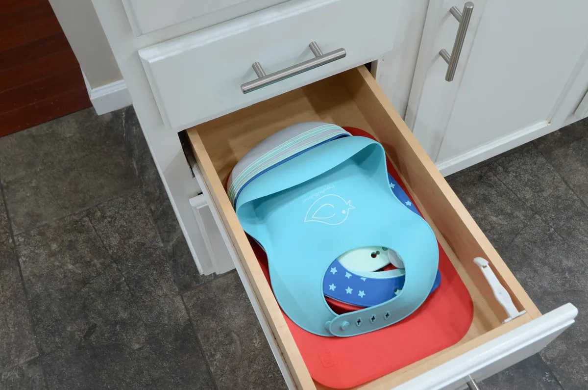 This image shows a neatly organized kitchen drawer filled with colorful bibs, set against clean cabinetry lines. The playful element of the bibs and the practical organization speaks to a household that accommodates young children and supports family mealtime routines.
