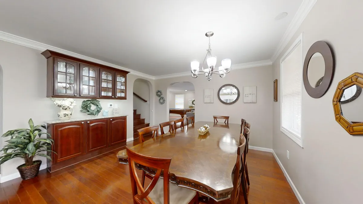 A warm, inviting dining area with a large table set for a group, illuminated by a chandelier. The wooden cabinet and decorative mirrors add a touch of elegance and festivity, evoking scenes of family gatherings and holiday celebrations.