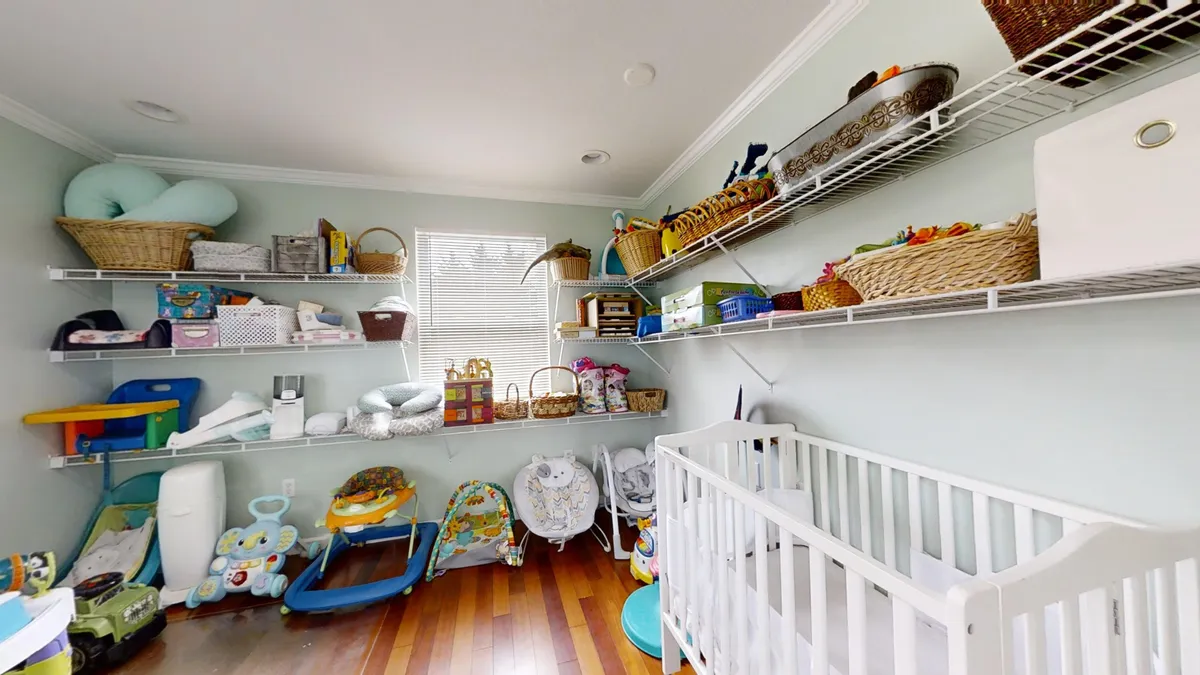 A cheerful nursery with a crib, shelves filled with toys and baby gear, and colorful baskets. The room radiates warmth and care, showing thoughtful accommodations for families with young children, from naptime to playtime.