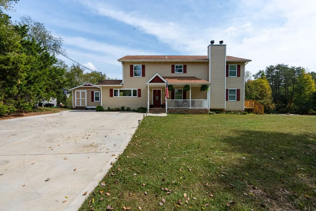 A two-story house with a charming front porch, a spacious driveway, and a lush garden area. The scene depicts a welcoming family home with space for children to play in the yard or families to gather on the porch. The environment is alive with possibilities for outdoor activities and togetherness.