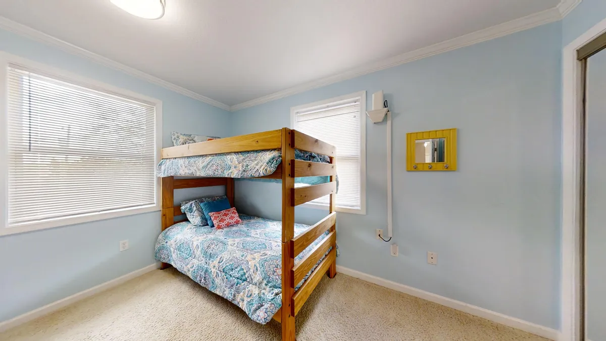 A kid-friendly bedroom with a bunk bed decked in colorful linens, a sunny window, a playful yellow mirror, and inviting décor. The arrangement encourages napping, reading, and imaginative play in a bright and appealing space.