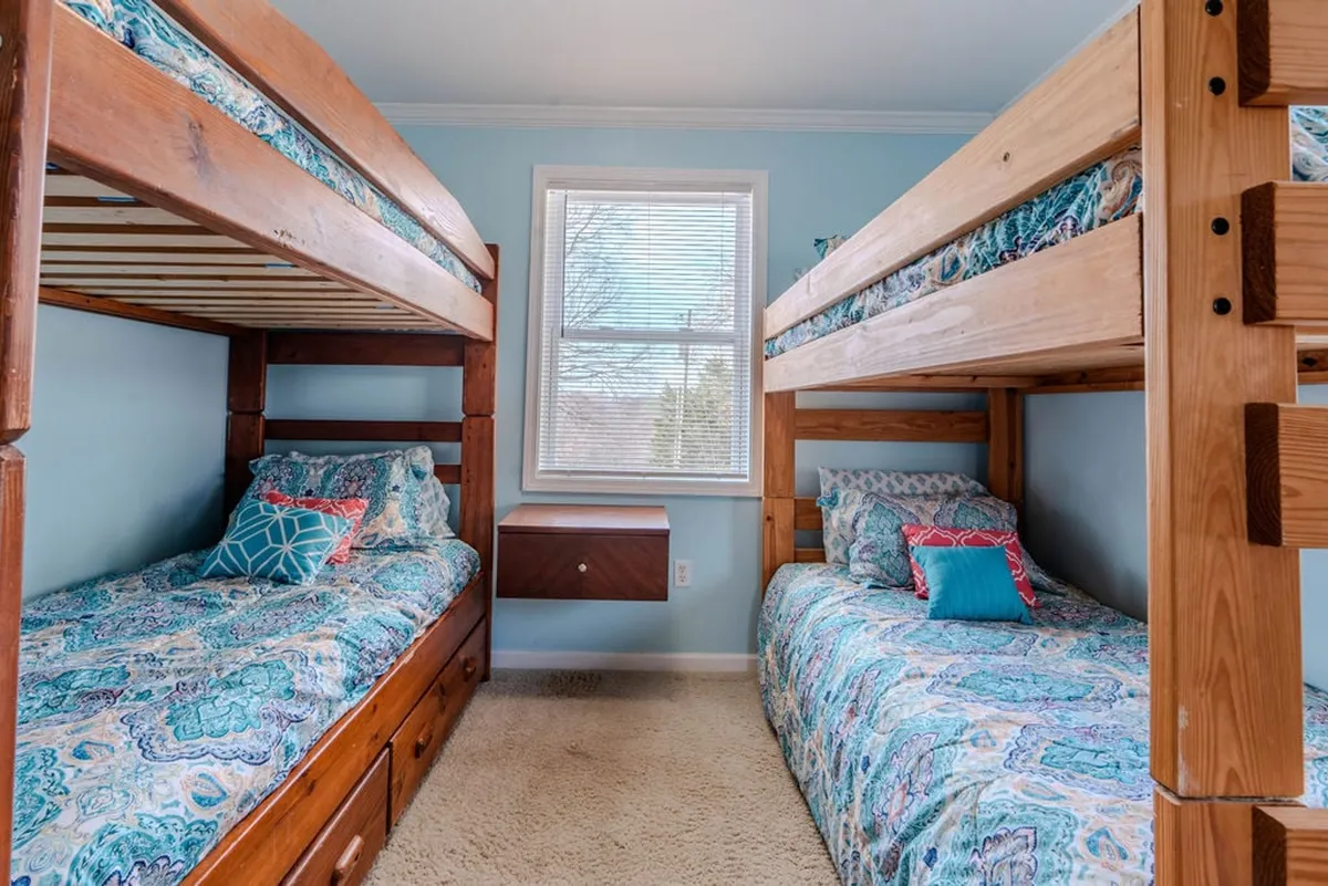 A cozy children's room featuring cheerful bunk beds with colorful bedding, bright lighting, and a window view. The playful atmosphere is evident, designed to accommodate sleep, reading, and playful moments for children.